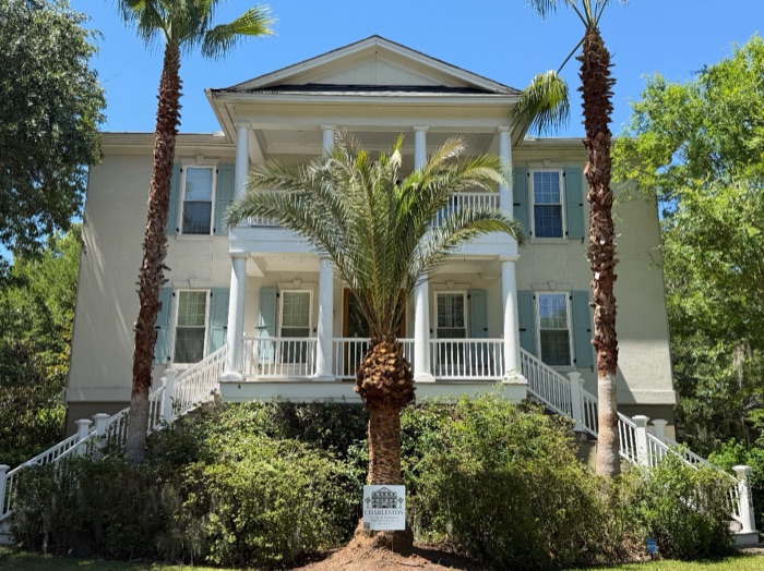 Two-story Charleston home with stacked front porches and white railings, framed by palm trees