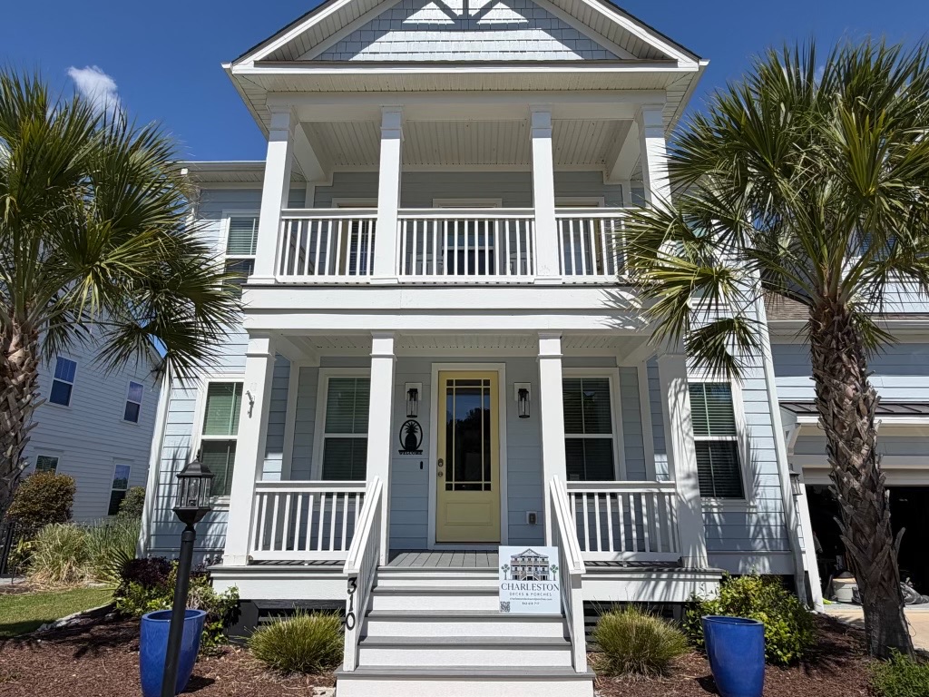 Newly built two-story Charleston home with stacked front porches, white railings, and a yellow front door